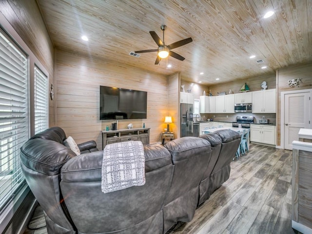 living room featuring light hardwood / wood-style floors, wooden ceiling, wood walls, and ceiling fan