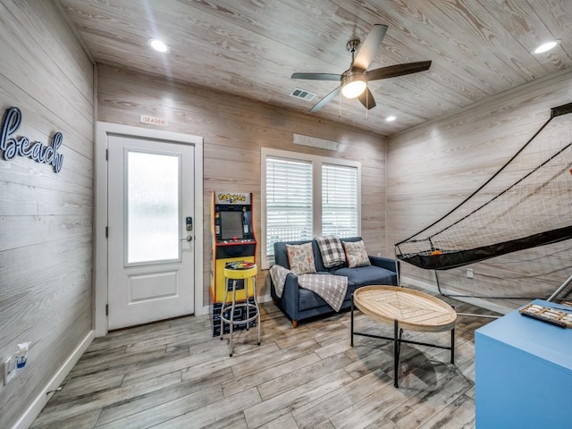 living area featuring ceiling fan, wooden ceiling, and wooden walls