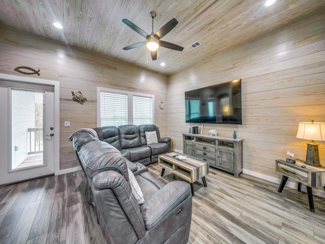 living room with wood walls, ceiling fan, light hardwood / wood-style floors, and plenty of natural light