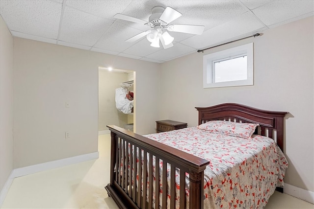 bedroom with a drop ceiling, ensuite bathroom, and ceiling fan