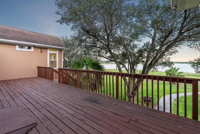 deck at dusk with a yard and a water view