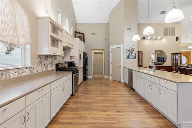 kitchen featuring light hardwood / wood-style floors, appliances with stainless steel finishes, decorative light fixtures, high vaulted ceiling, and white cabinets