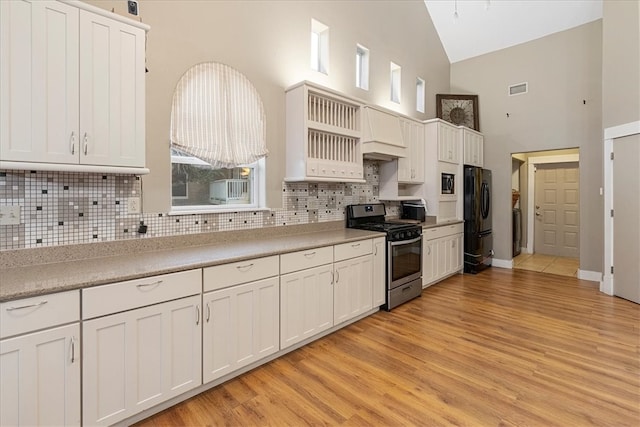 kitchen with light hardwood / wood-style floors, black fridge, stainless steel range oven, high vaulted ceiling, and white cabinetry