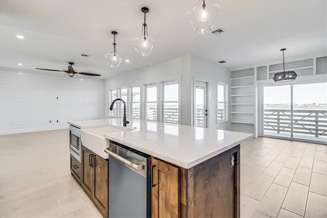 kitchen featuring dishwasher, hanging light fixtures, plenty of natural light, a center island with sink, and built in shelves