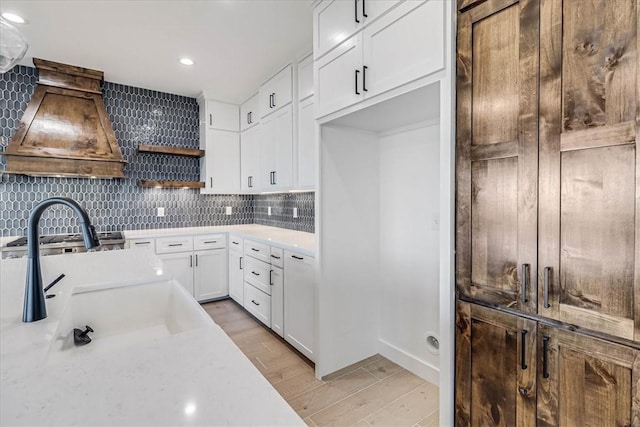 kitchen featuring premium range hood, sink, light hardwood / wood-style flooring, white cabinets, and backsplash