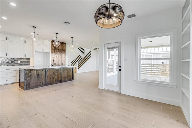 kitchen with hanging light fixtures, decorative backsplash, an island with sink, and white cabinets