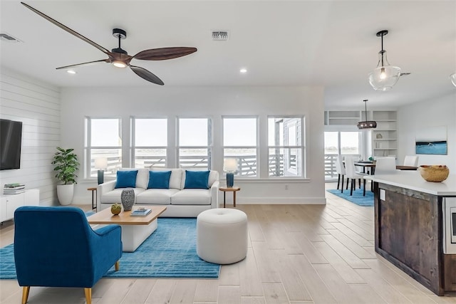 living room with ceiling fan, wooden walls, and light wood-type flooring