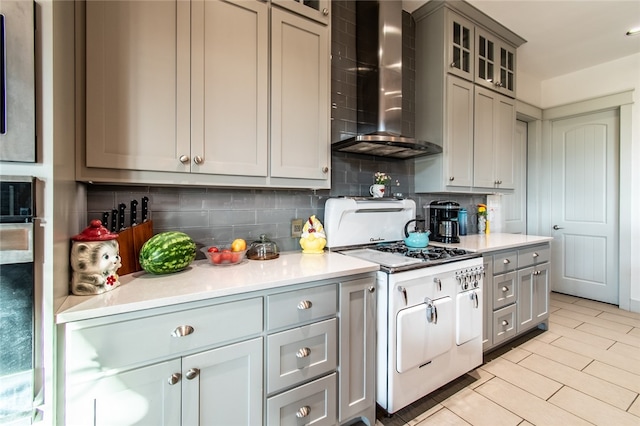 kitchen featuring white range with gas cooktop, decorative backsplash, gray cabinets, and wall chimney range hood