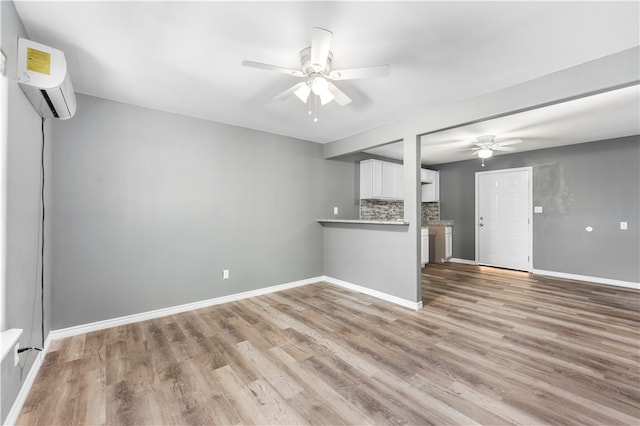 unfurnished living room featuring a wall unit AC, ceiling fan, and light wood-type flooring