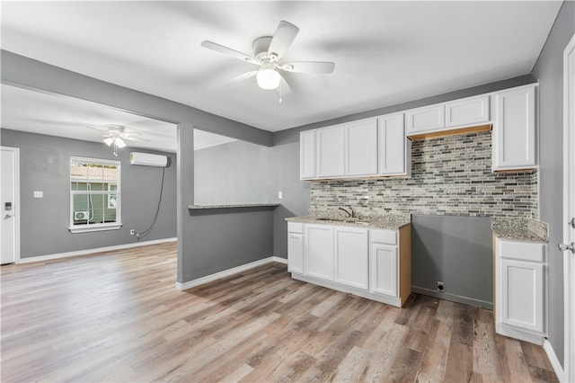 kitchen with white cabinets, light wood-type flooring, a wall mounted air conditioner, and sink