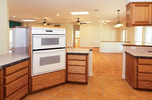 kitchen featuring tile countertops, light tile patterned flooring, ceiling fan, hanging light fixtures, and white double oven