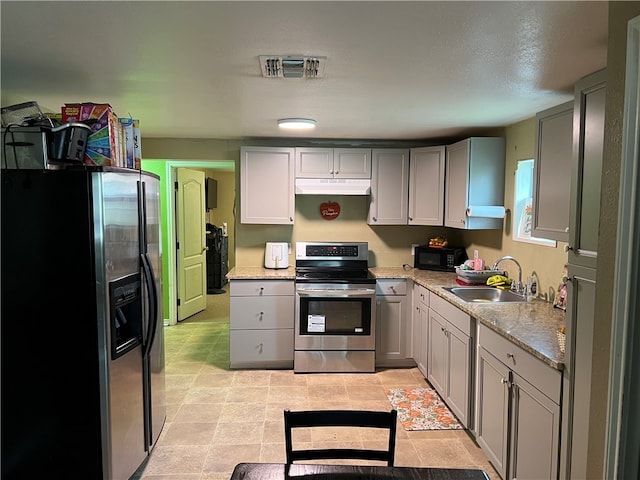 kitchen with gray cabinets, appliances with stainless steel finishes, sink, and light stone countertops