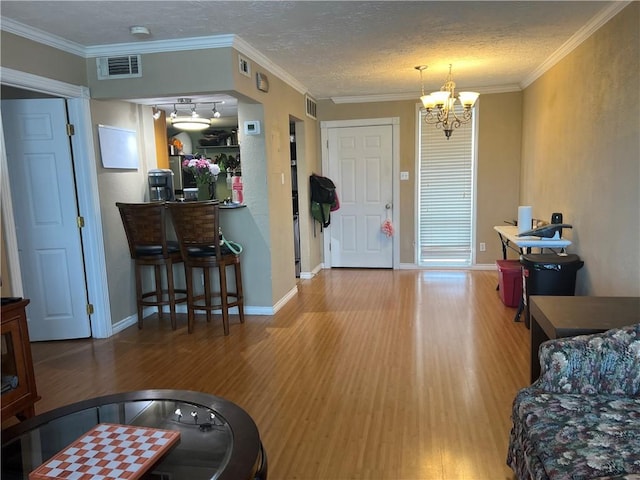 entryway featuring visible vents, a notable chandelier, ornamental molding, a textured ceiling, and wood finished floors