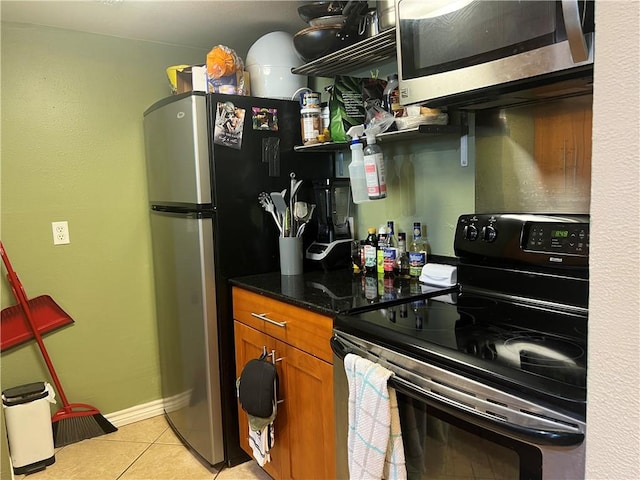 kitchen featuring light tile patterned flooring, stainless steel appliances, brown cabinetry, and baseboards