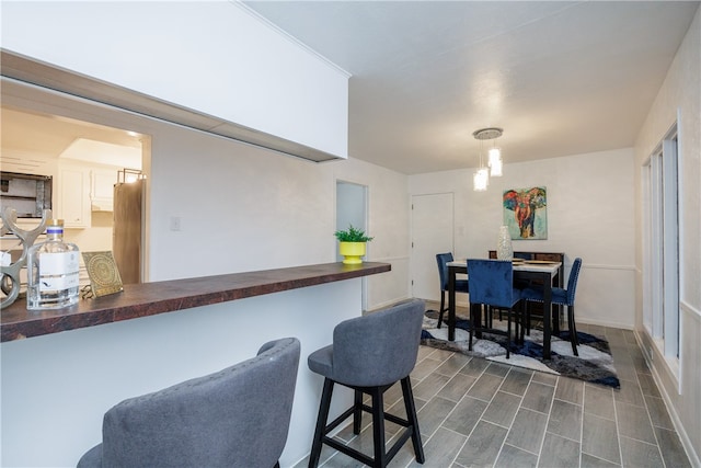 kitchen featuring a kitchen breakfast bar, stainless steel fridge, white cabinets, and pendant lighting