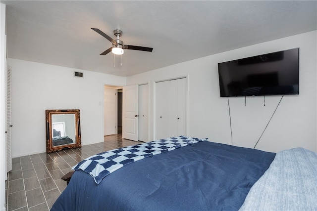 bedroom with dark hardwood / wood-style flooring, two closets, and ceiling fan