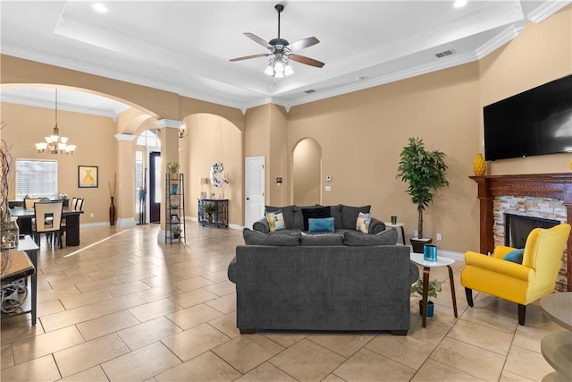 living room with a tray ceiling, arched walkways, a fireplace, visible vents, and ceiling fan with notable chandelier