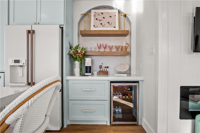 bar with a dry bar, wine cooler, white refrigerator with ice dispenser, and wood finished floors