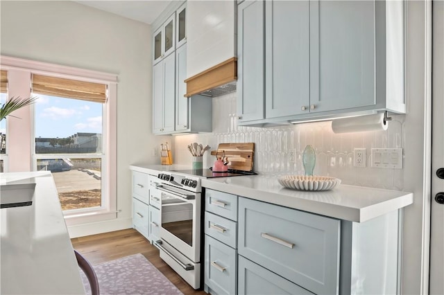 kitchen featuring wood finished floors, light countertops, backsplash, electric range oven, and glass insert cabinets