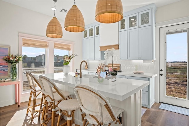 kitchen with an island with sink, visible vents, light countertops, and dark wood-type flooring