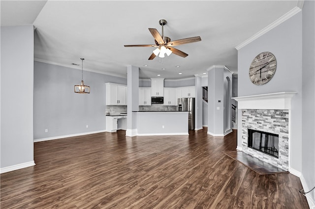 unfurnished living room featuring a stone fireplace, dark wood-type flooring, ornamental molding, and ceiling fan