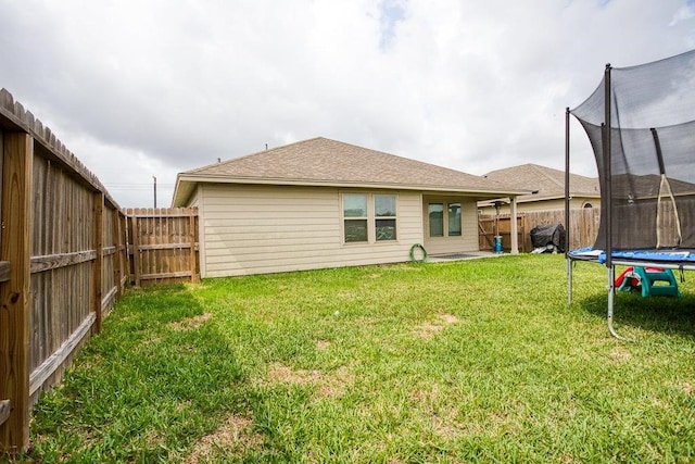 rear view of property featuring a trampoline, a fenced backyard, and a yard