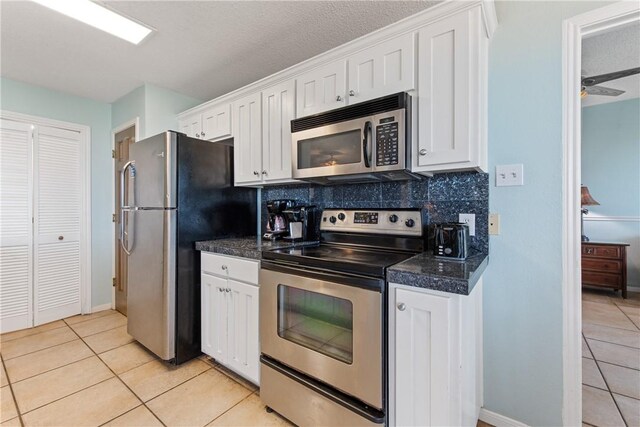 kitchen with dark countertops, white cabinets, light tile patterned floors, and stainless steel appliances