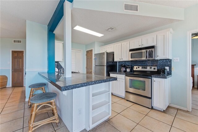 kitchen featuring visible vents, tile countertops, white cabinets, and stainless steel appliances