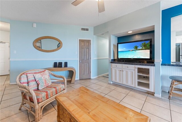 living room with light tile patterned floors, visible vents, baseboards, and a ceiling fan