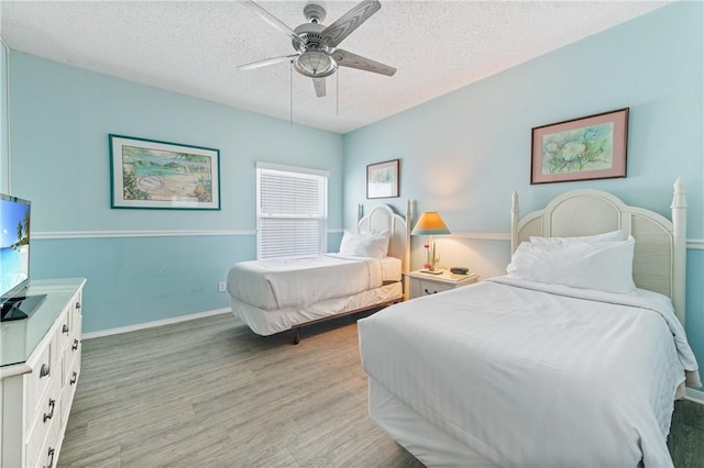 bedroom with light wood finished floors, a textured ceiling, baseboards, and a ceiling fan