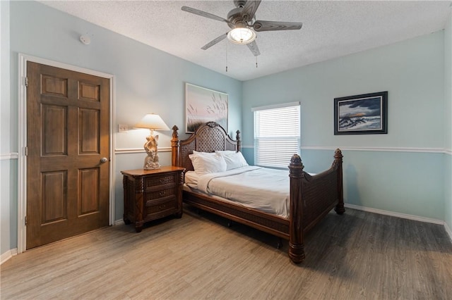 bedroom with a textured ceiling, light wood-type flooring, baseboards, and a ceiling fan