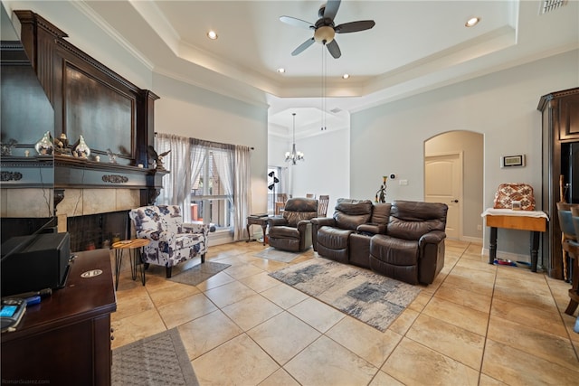 tiled living room featuring ornamental molding, ceiling fan with notable chandelier, a fireplace, and a tray ceiling