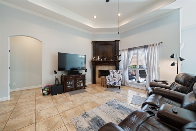 living room featuring light tile patterned flooring, a tiled fireplace, a raised ceiling, and ornamental molding