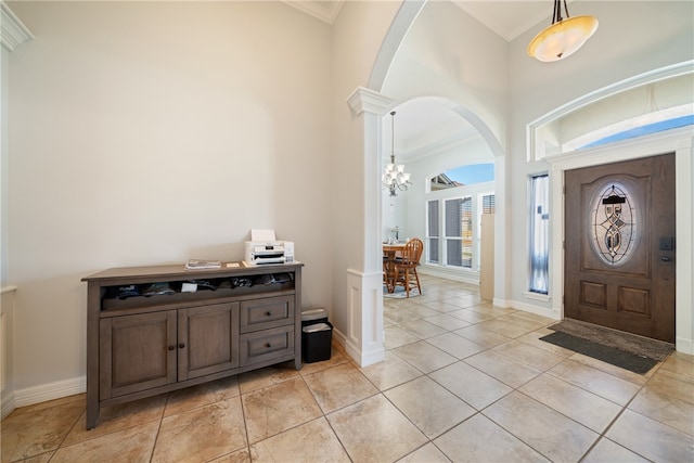 tiled entrance foyer with a towering ceiling, a chandelier, crown molding, and decorative columns