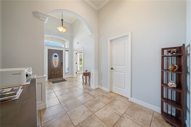 foyer entrance with light tile patterned floors, a towering ceiling, ornate columns, and crown molding