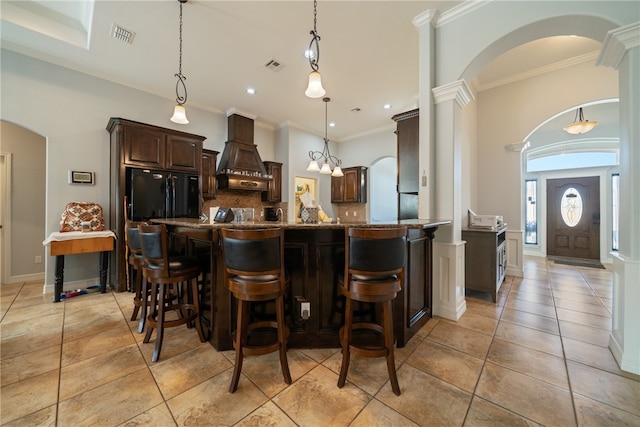 kitchen featuring a center island, decorative backsplash, dark brown cabinetry, custom range hood, and decorative light fixtures