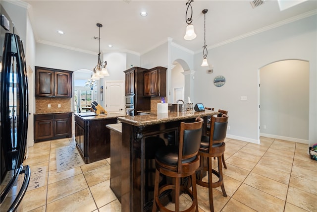 kitchen featuring an island with sink, dark brown cabinets, black fridge, and decorative backsplash