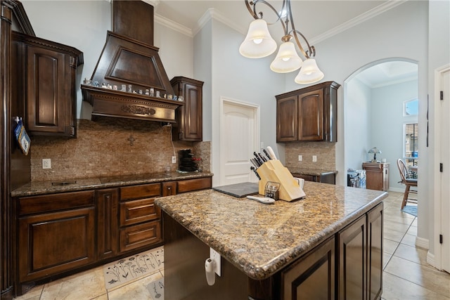 kitchen with ornamental molding, decorative light fixtures, dark brown cabinets, stone counters, and a center island