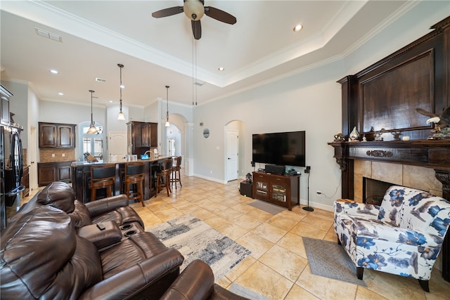 tiled living room featuring ornamental molding, a tiled fireplace, and ceiling fan