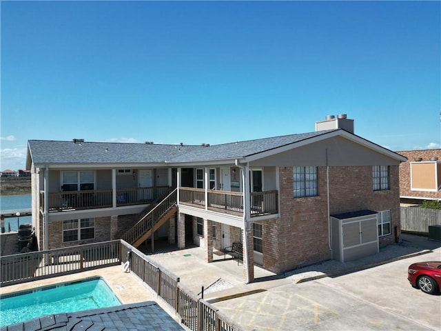 back of house featuring brick siding, a patio, a community pool, and fence