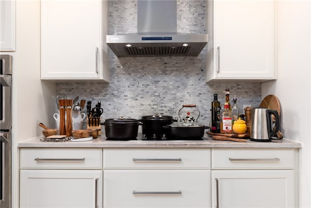 kitchen featuring black electric cooktop, wall chimney exhaust hood, white cabinetry, and backsplash