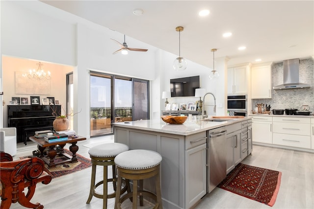 kitchen featuring stainless steel appliances, wall chimney range hood, light wood-type flooring, a high ceiling, and a kitchen island with sink