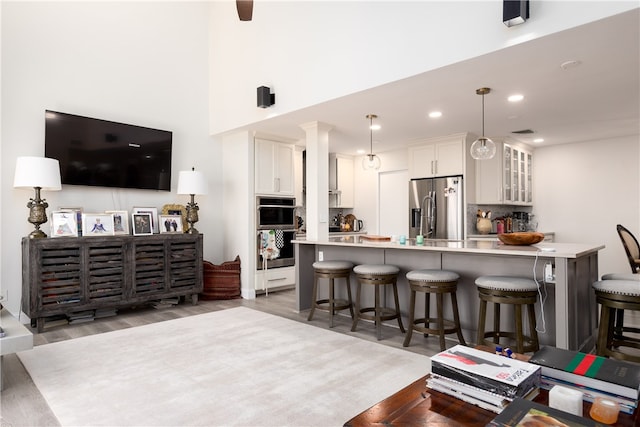 kitchen featuring stainless steel appliances, decorative light fixtures, a kitchen bar, white cabinets, and light hardwood / wood-style flooring