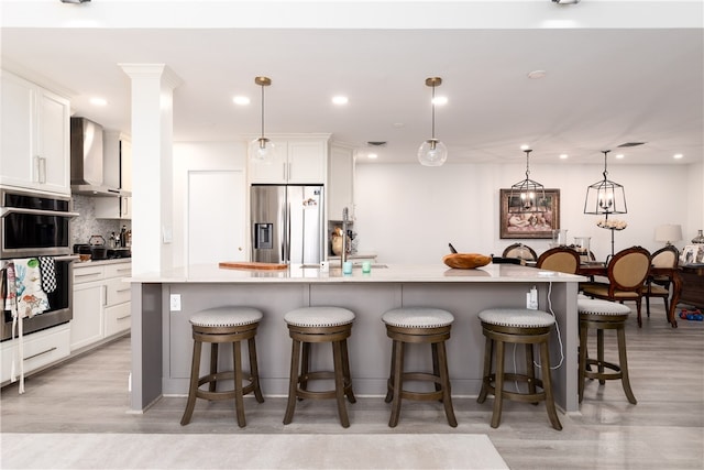 kitchen with wall chimney exhaust hood, a breakfast bar, pendant lighting, appliances with stainless steel finishes, and a large island with sink