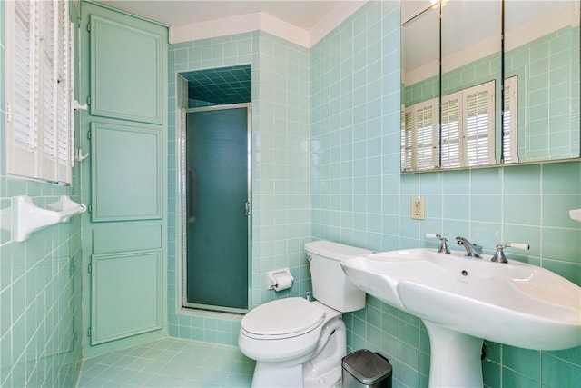 bathroom featuring sink, toilet, a shower with door, and tile walls