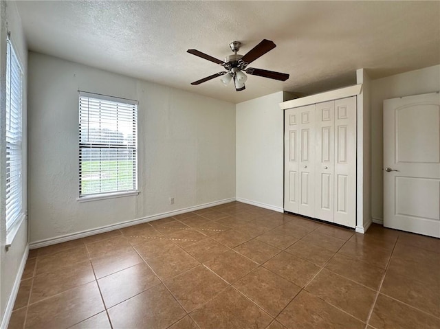 unfurnished bedroom with ceiling fan, a closet, tile patterned floors, and a textured ceiling