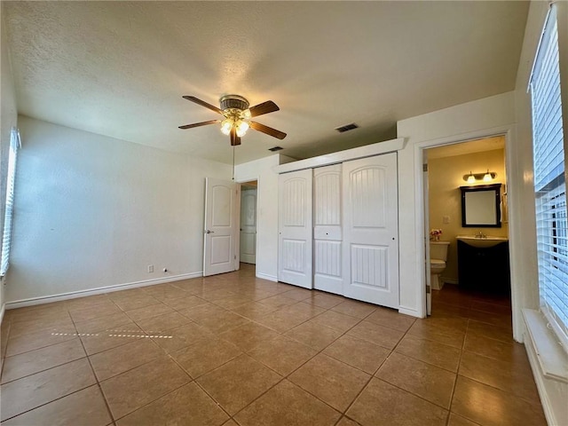 unfurnished bedroom with ensuite bathroom, tile patterned flooring, ceiling fan, a textured ceiling, and a closet