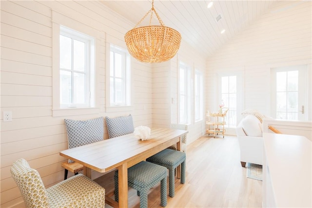 dining area with a healthy amount of sunlight, light wood-style flooring, vaulted ceiling, and a notable chandelier
