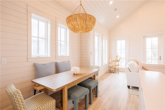 dining room featuring lofted ceiling, wooden ceiling, wooden walls, breakfast area, and light hardwood / wood-style floors