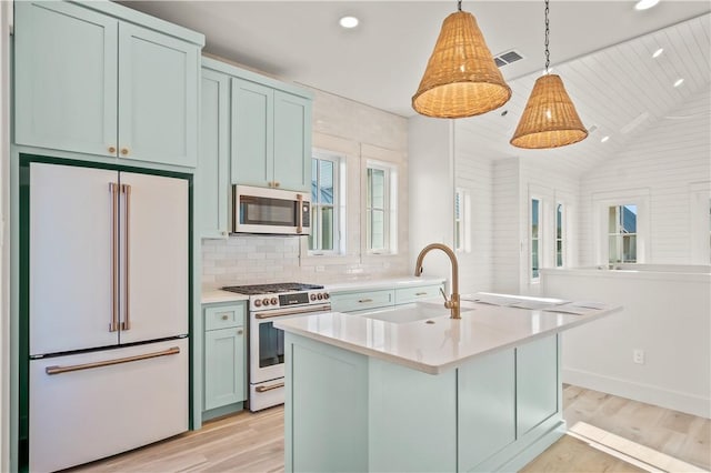 kitchen featuring high end appliances, a kitchen island with sink, sink, hanging light fixtures, and light wood-type flooring